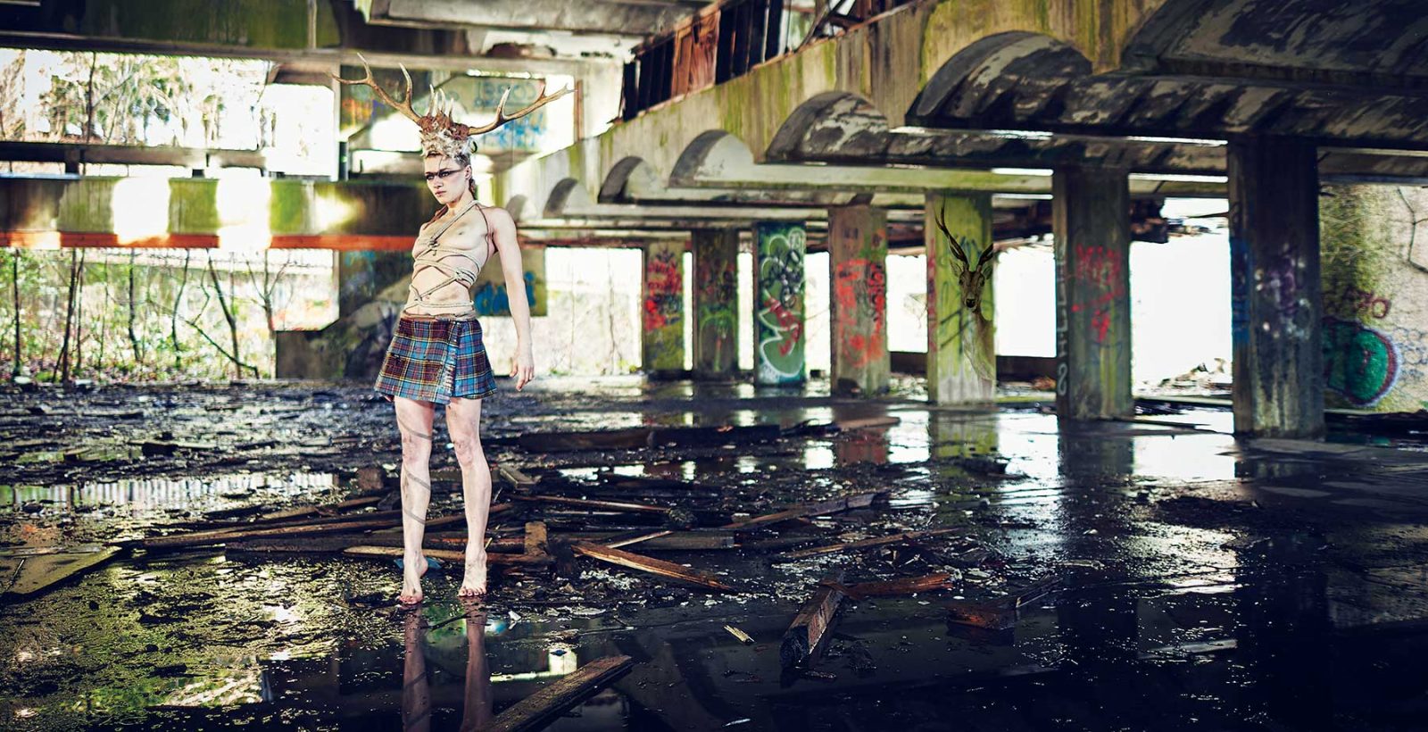 In-between book-your-warrior-guide -warrior sister in an abandoned building wearing a mini kilt, rope binding and stag antlers on her head