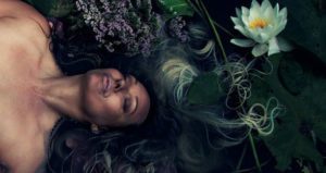 a woman lies in water with water lilies floating around her